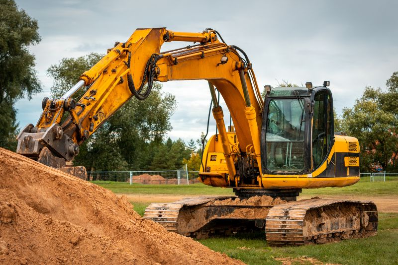 a yellow excavator moving a pile of soil